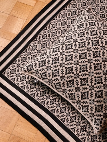 Pillows and blankets from the Dale of Norway Home collection, displayed stacked on a stool, in a close-up on the floor, and draped over a bench